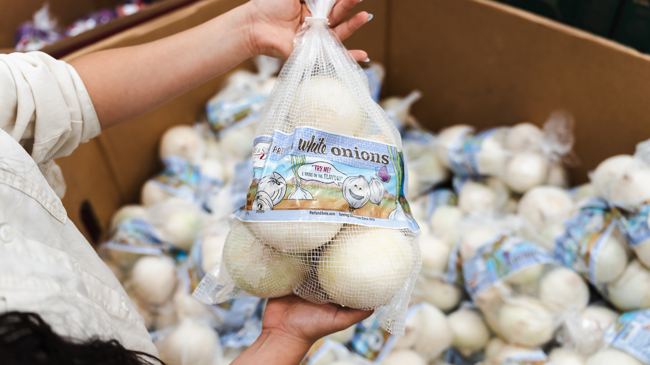 Shopper holding a white mesh onion bag in a grocery store produce section