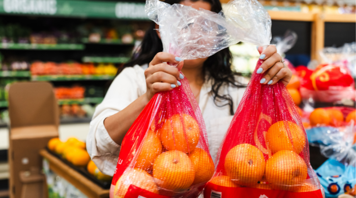 Customer holding a branded mesh bag of oranges in a retail produce aisle